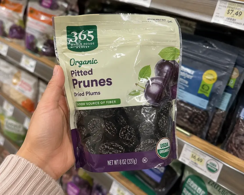 Prune puree for baby starts with quality organic dried prunes, shown in a resealable bag with dark pitted prunes visible on a grocery store shelf.