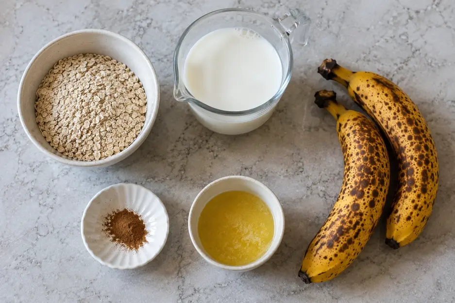 Banana oat pancakes for baby ingredients including rolled oats, ripe spotted bananas, milk, cinnamon, and melted butter arranged on a kitchen countertop.
