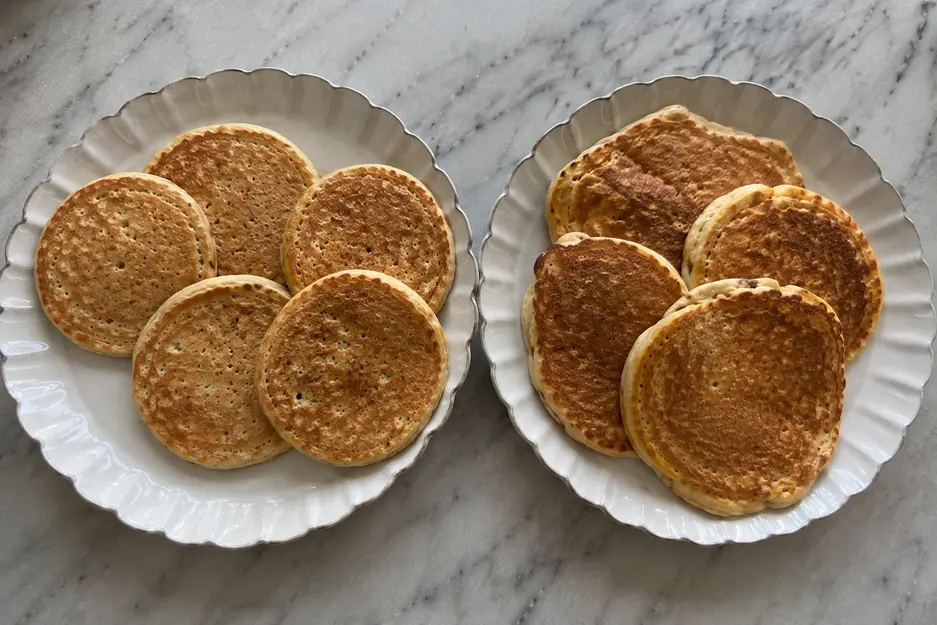 Banana oat pancakes for baby shown in two batches, with egg-free pancakes beside egg-included oat pancakes on matching cream plates in natural kitchen light.