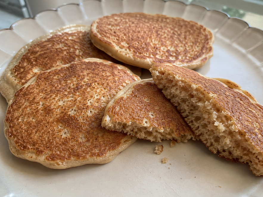 Banana oat pancakes for baby cooling on a cream plate, with one golden pancake torn open to show its soft, moist, fully cooked oat center.