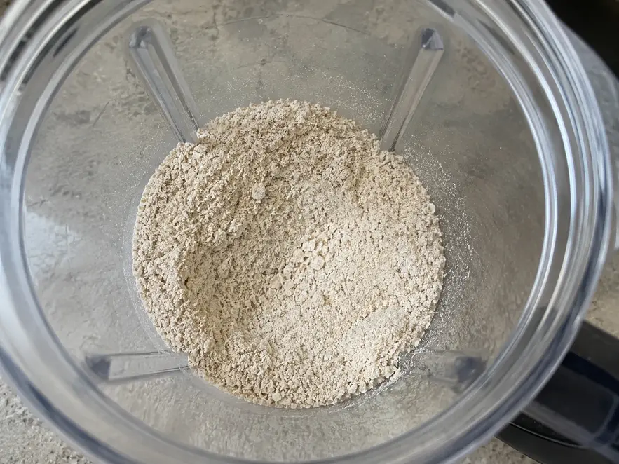 Banana oat pancakes for baby preparation showing finely ground oats inside a clear blender jar with small oat flecks visible in natural kitchen light.