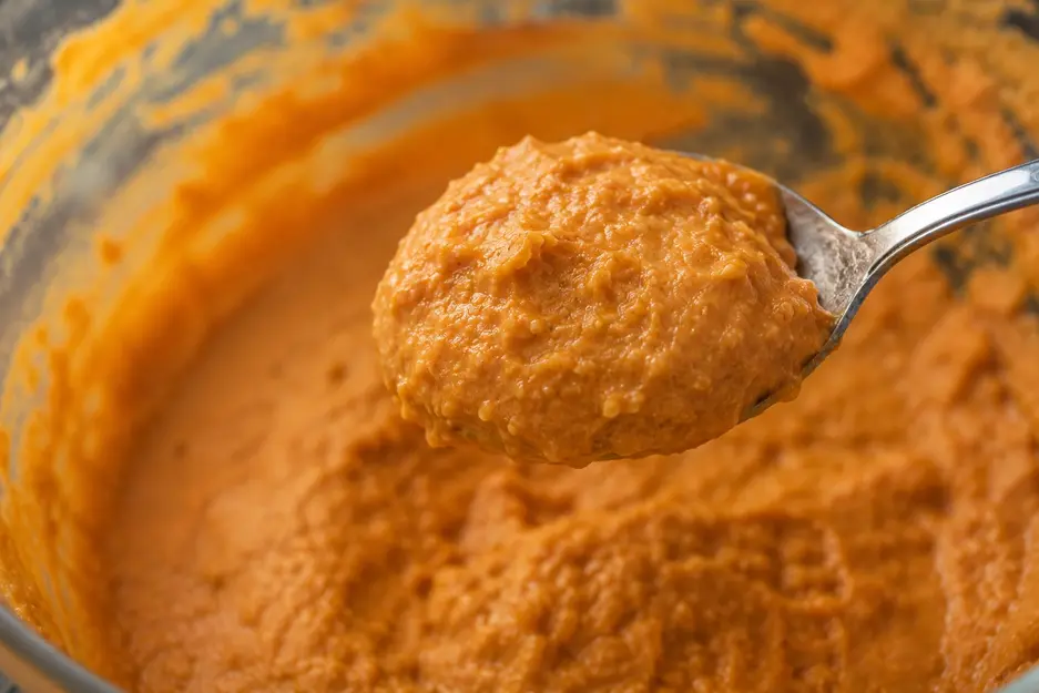 Thick sweet potato pancake batter holding its shape on a spoon, showing the ideal consistency for baby led weaning pancakes.