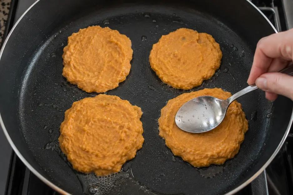 Sweet potato pancake batter being shaped and flattened in a skillet to make soft baby led weaning pancakes.