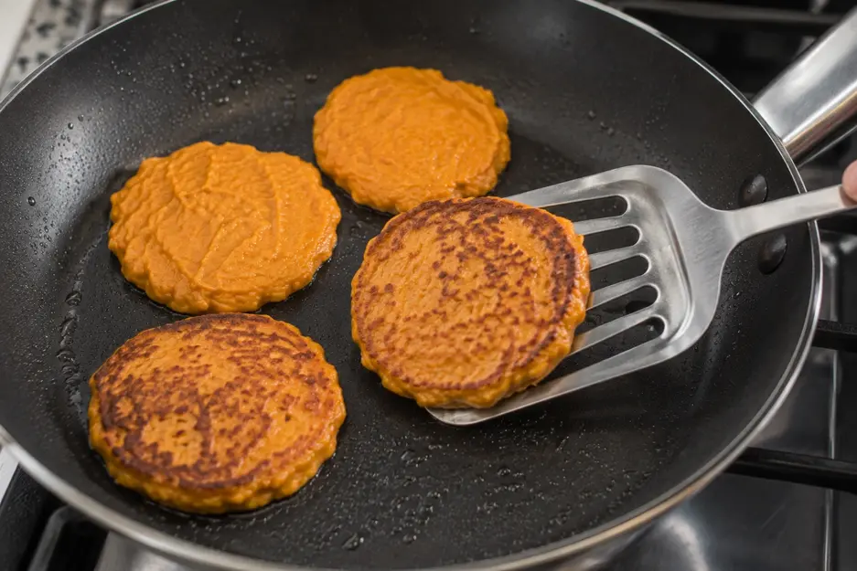 Sweet potato pancakes for baby led weaning being flipped in a skillet, showing naturally golden cooked surfaces and soft homemade texture.