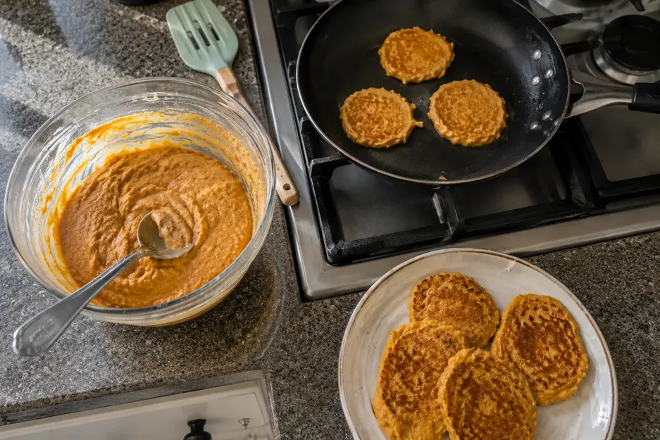 Sweet potato pancakes for baby led weaning cooking in a skillet with thick homemade batter and freshly cooked pancakes ready to serve.