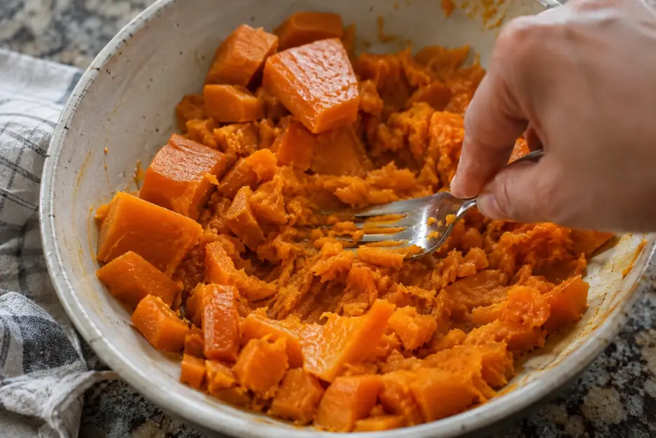 Cooked sweet potato cubes being mashed with a fork to prepare soft sweet potato pancakes for baby led weaning.