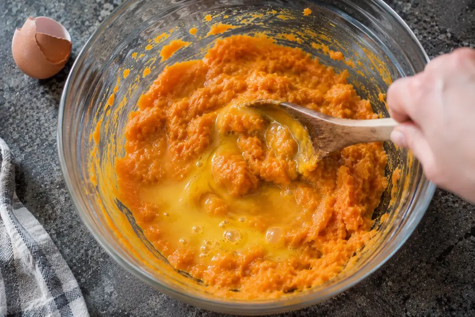 Egg being mixed into mashed sweet potato for sweet potato pancakes for baby led weaning, creating a soft homemade pancake batter.