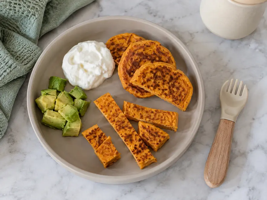 Sweet potato pancakes for baby led weaning cut into easy-to-grasp pieces and served with plain yogurt and soft avocado.